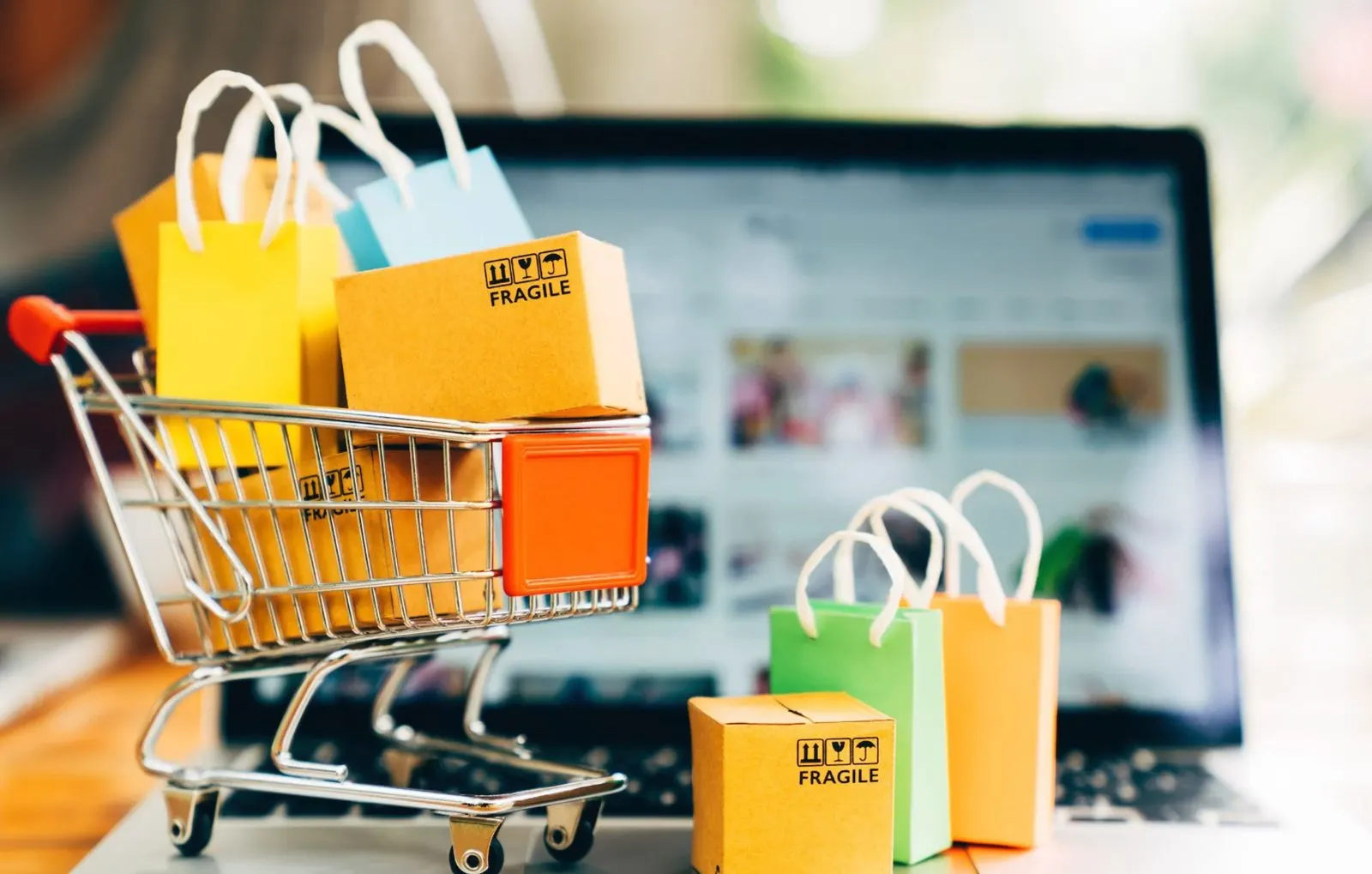 Online marketplace order — a cart of parcels and shopping bags on a laptop